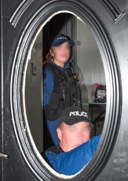 Two police officers inside a home repairing a damaged door frame.