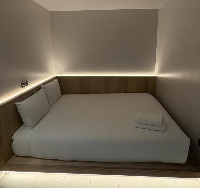 A bed built into a wooden platform, lit from below and behind the headboard by strip lighting.