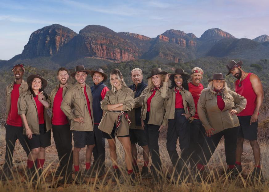 Cast of "I'm a Celebrity... Get Me Out of Here! South Africa" posing in safari outfits in front of mountains.