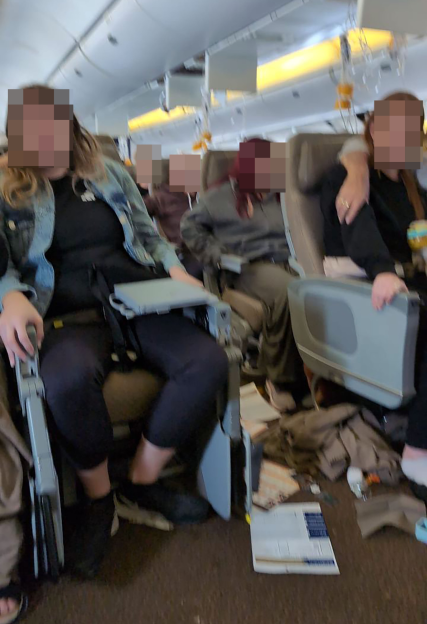 Several people, some using mobility devices, are seated in an airplane cabin.