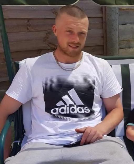 Astron Inman sitting outdoors, wearing a white t-shirt and light gray sweatpants.