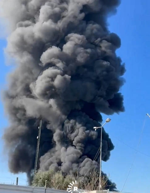 Thick black smoke rising into a clear blue sky.