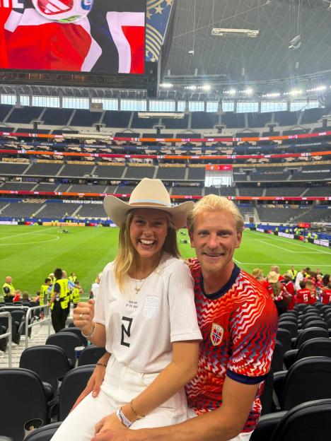 A man and woman wearing soccer jerseys sitting in stadium stands.