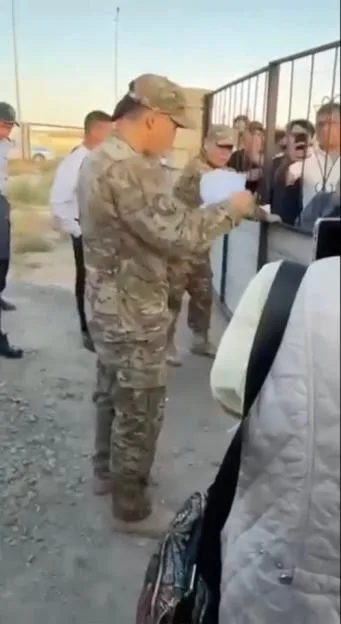 A serviceman reads a list of names to a crowd behind a gate.