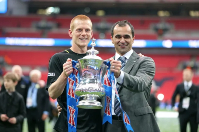 Two men smiling, holding the FA Cup trophy together.