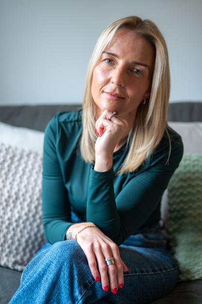 Marnie Dillon, a blonde woman in a teal shirt and jeans, sitting on a couch.