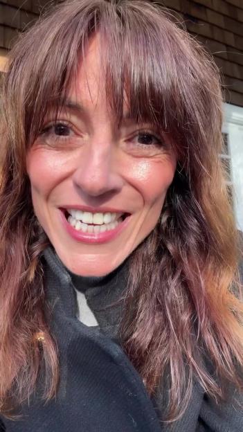 A woman with long brown hair smiles widely, showing her teeth.