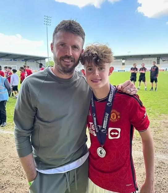A man and a boy in a Manchester United jersey with a medal around his neck pose together on a soccer field.