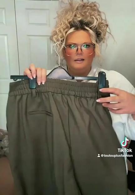 A woman holds up a pair of olive green Tesco F&F plus-size trousers.