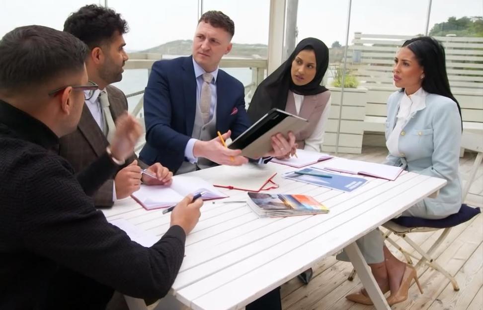 Five candidates from The Apprentice seated around a white table.