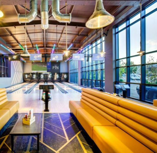 A modern bowling alley with six lanes, yellow leather seating, and large windows.