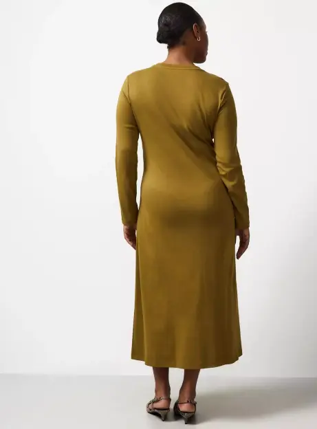 Back view of a woman wearing a long-sleeved, ankle-length olive green dress and snakeskin print heels.