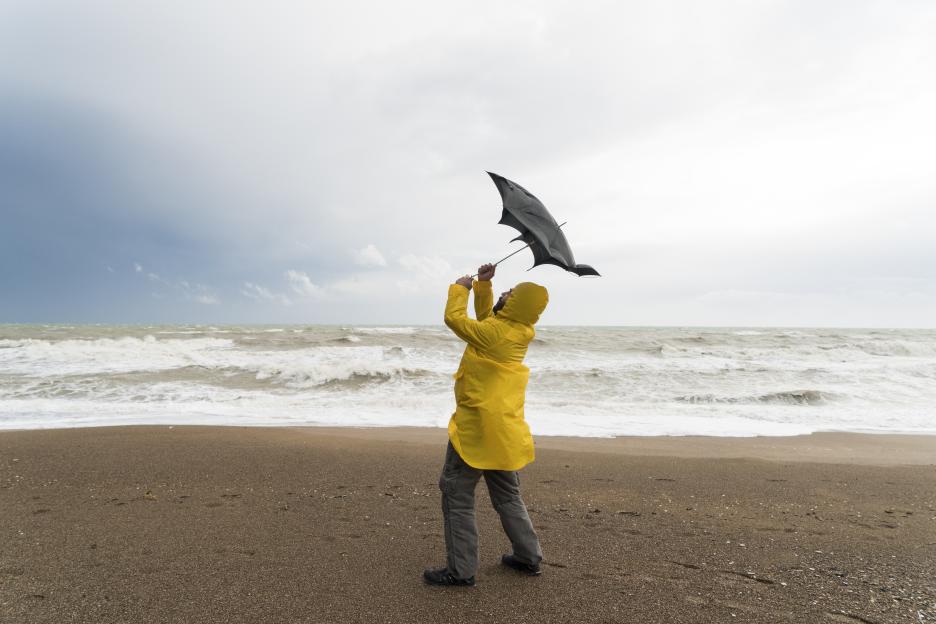 Man on a stormy beach with a broken umbrella.