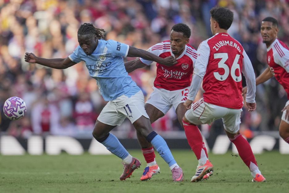 Manchester City's Jeremy Doku and Arsenal's Jurrien Timber fighting for the ball during a soccer match.