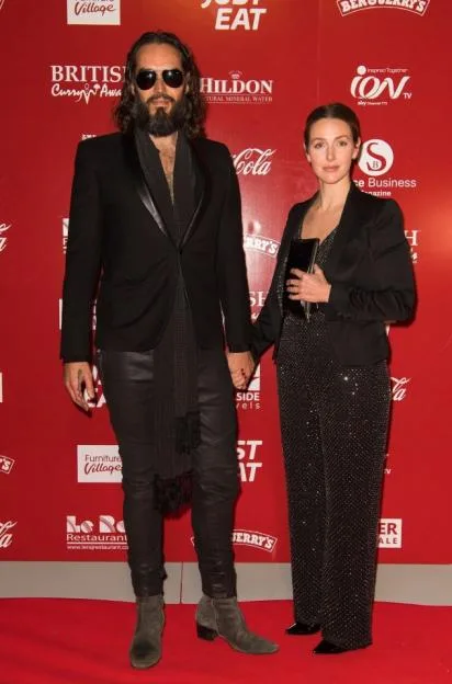 Russell Brand and Laura Gallacher pose together on a red carpet.