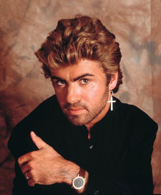 Studio portrait of George Michael in a black shirt with a cross earring and a watch.