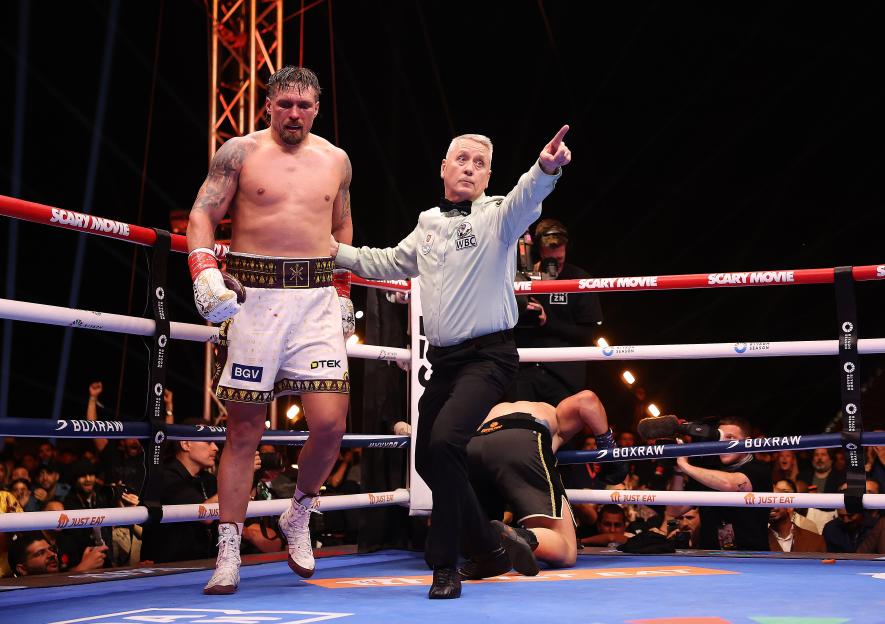 A boxer stands in the ring with a referee pointing, while another boxer lies on the mat, during a fight in Giza.