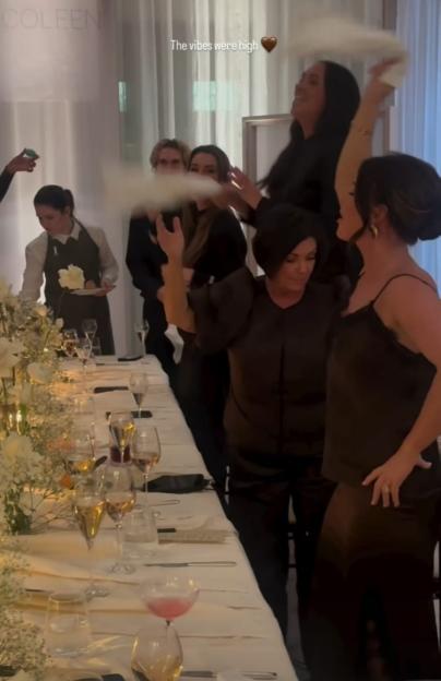 People dancing and waving white napkins over a long table set with wine glasses and white floral arrangements.
