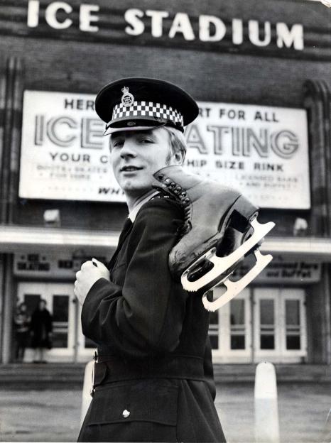 Ice-skater Christopher Dean in police uniform carrying ice skates at Ice Stadium.
