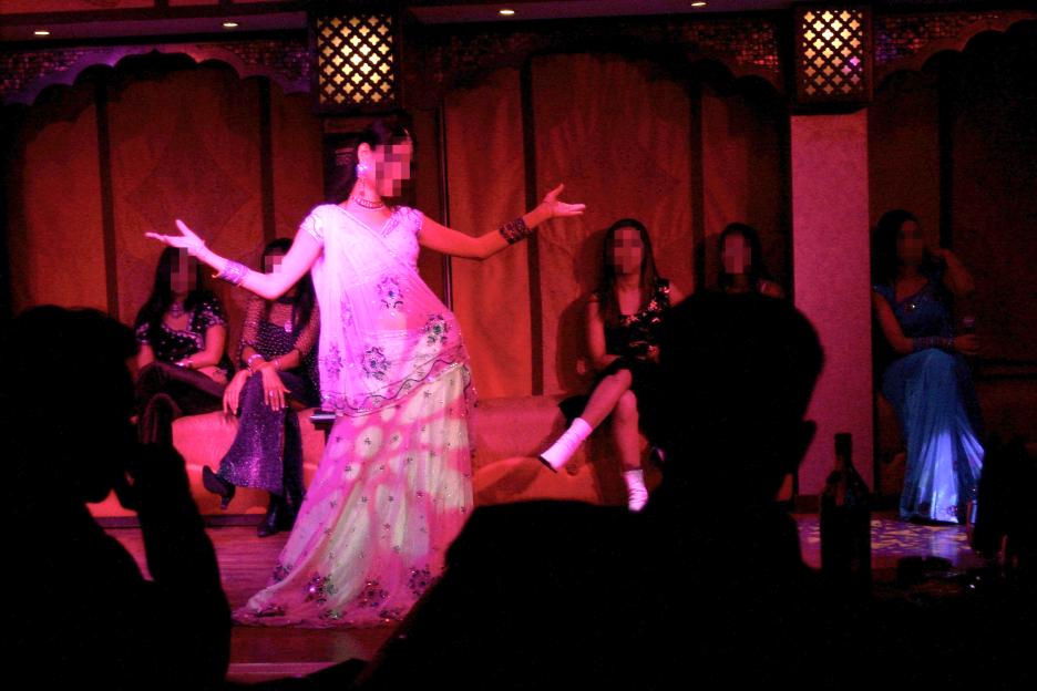 A woman in traditional attire dancing in front of an audience, blurred for privacy.
