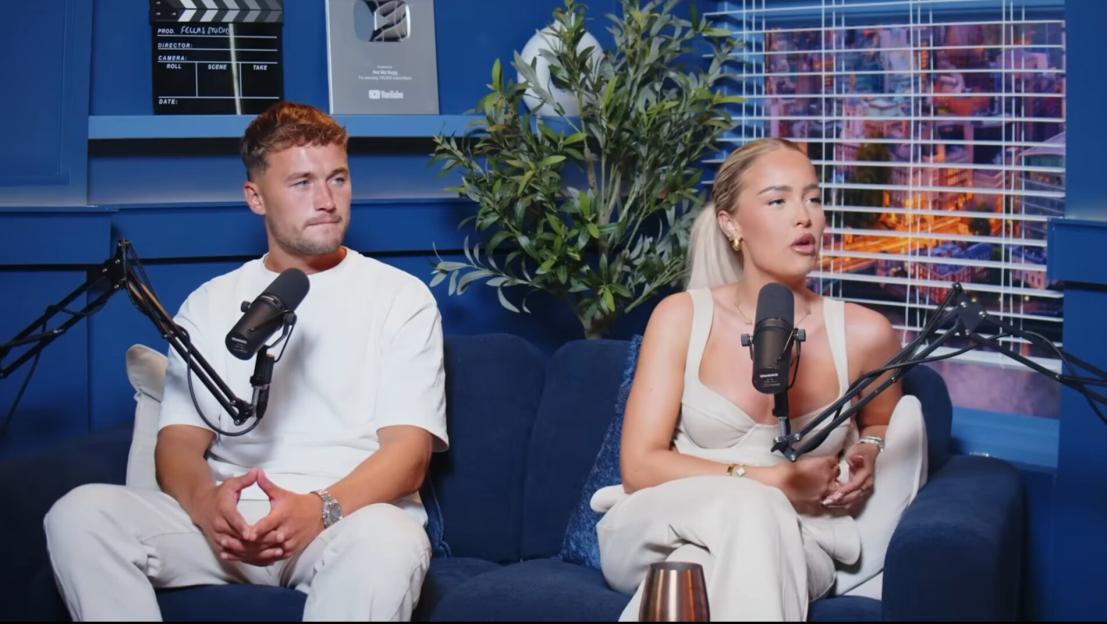 Love Island's Ellie and Finley sitting on a blue couch in front of microphones.