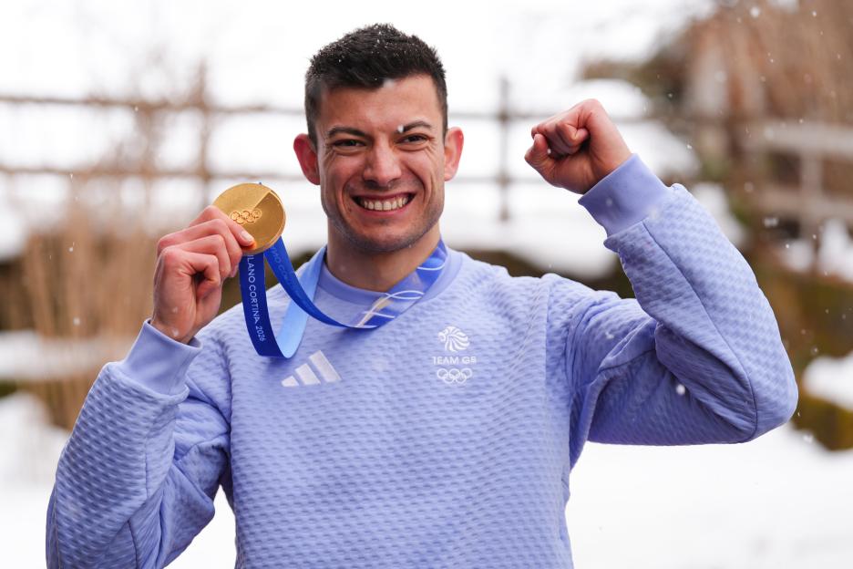 Matt Weston, Great Britain's Skeleton gold medalist, smiling and holding his medal with a raised fist.