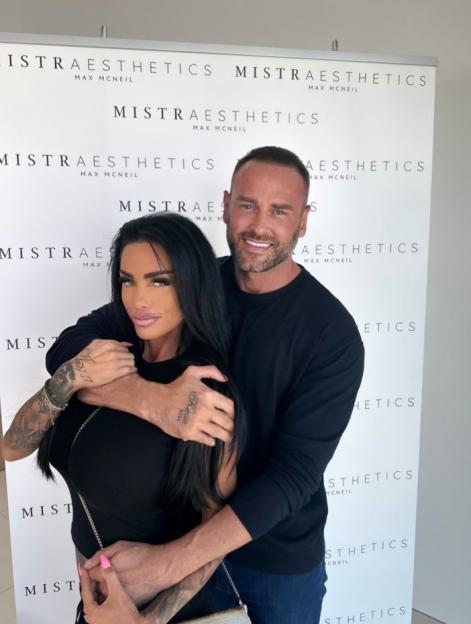 Katie Price and Carl Woods pose in front of a "Mistra Aesthetics" banner.