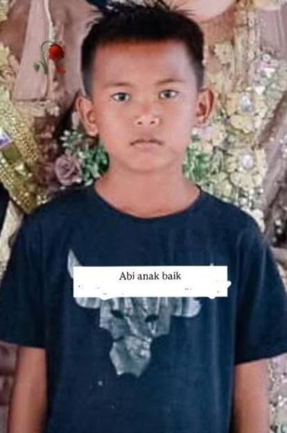 A young boy in a blue t-shirt with text "Abi anak baik" in white on it.