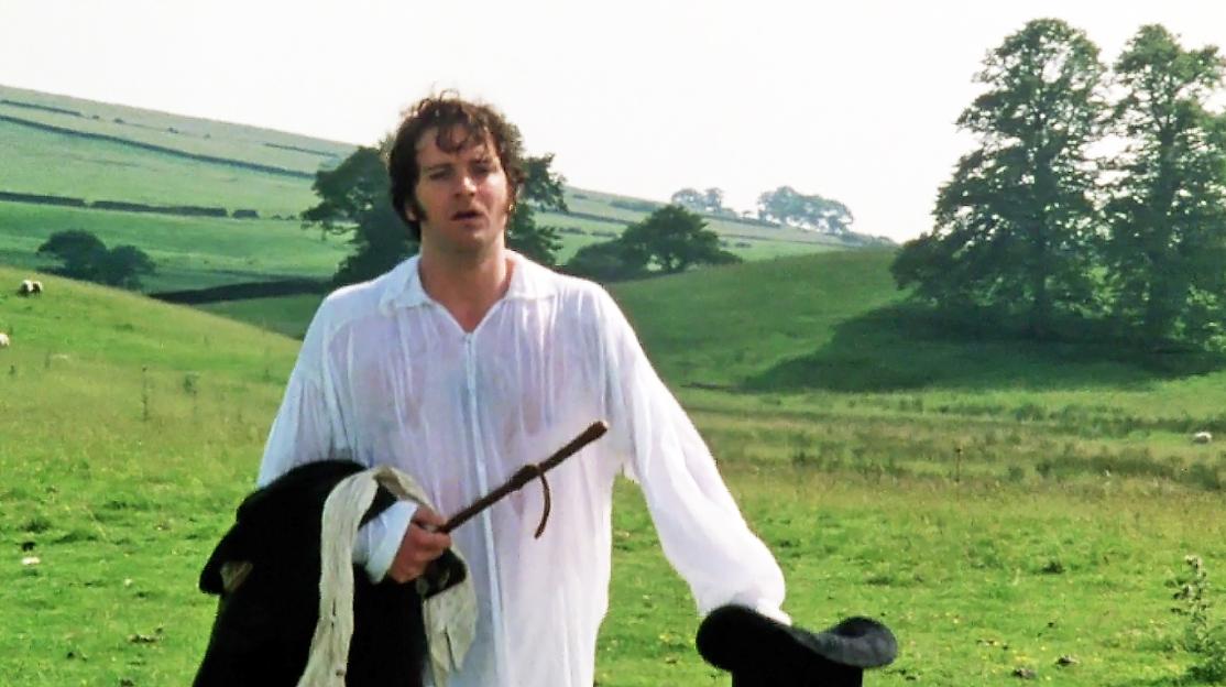 Colin Firth as Mr. Darcy, in a wet white shirt, holding a coat and riding crop in a green field.