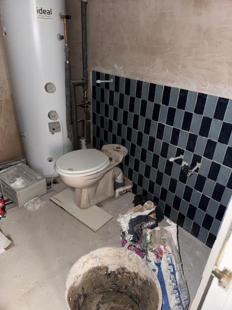 A toilet and water heater in a damaged room with construction materials on the floor.