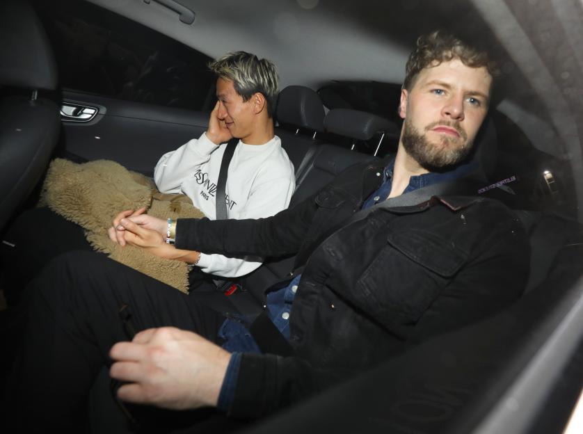 Carlos Gu and Jay McGuinness holding hands in the back of a car.