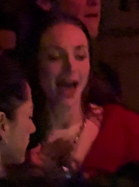 Sophie Turner partying, in a red top and gold necklace, with another person visible.