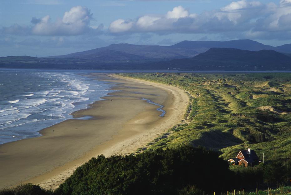 View of the Cambrian Coast with a sandy beach and a house nestled in dunes.