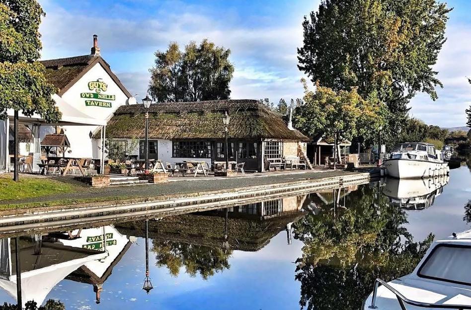 Owd Nells Tavern pub in Preston with a thatched roof sits next to a canal with boats.