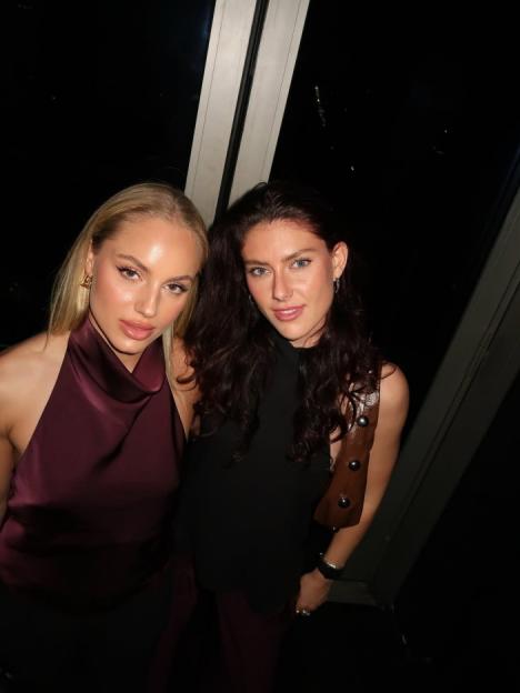 Two women posing for a photo at night, one with blonde hair and a maroon top, and the other with dark hair and a black top.