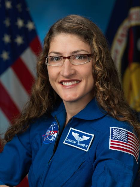 Astronaut Christina Hammock Koch smiling in a blue flight suit with NASA and US flag patches.