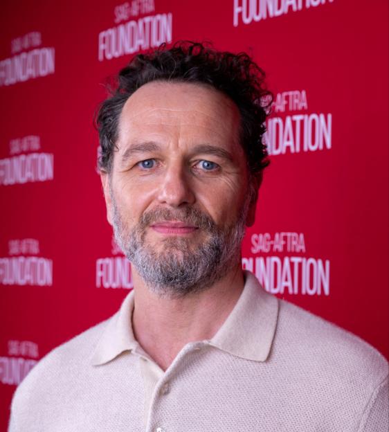 Matthew Rhys with a beard, wearing a light-colored polo shirt, against a red background with white "SAG-AFTRA FOUNDATION" logos.