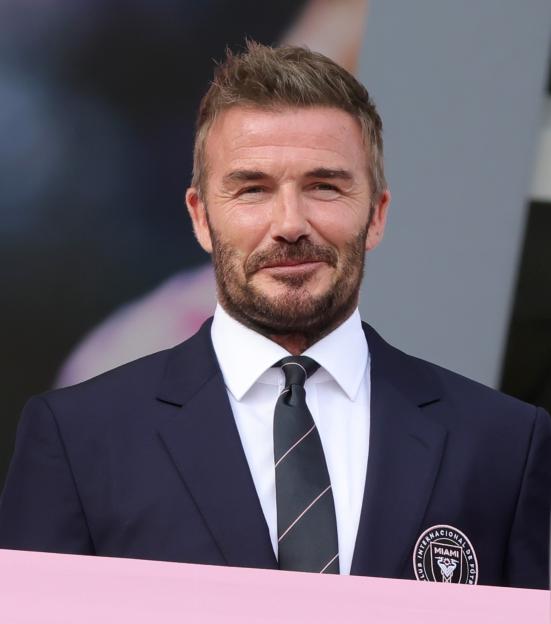 David Beckham in a suit and tie, wearing an Inter Miami CF badge.