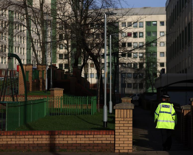 Police officer in a high-visibility jacket walking away from the camera in Lancashire Hill, Stockport.