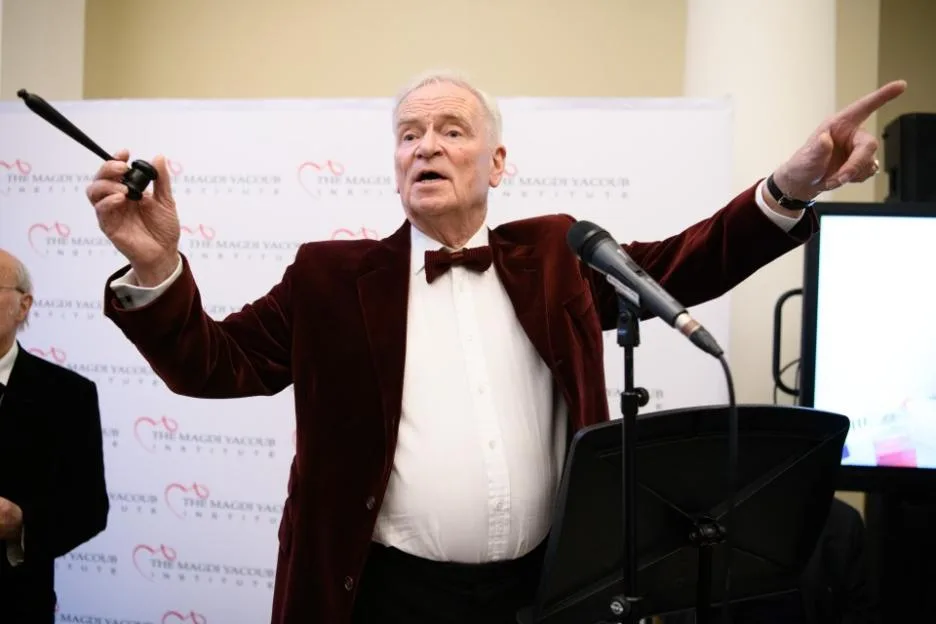 Lord Jeffrey Archer speaks passionately with outstretched arms while holding a gavel during an event.