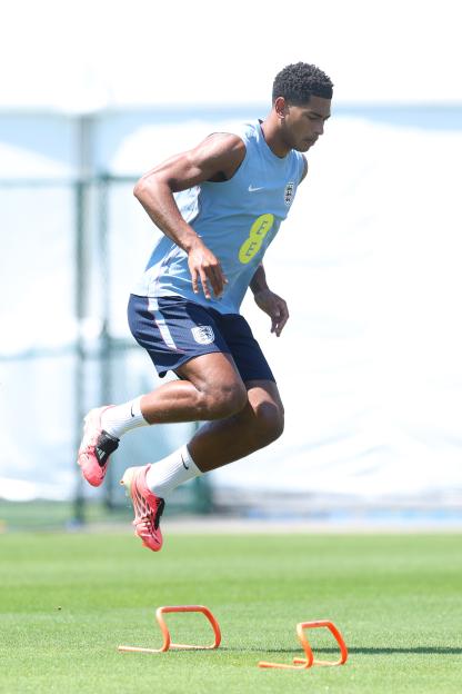 Jude Bellingham, wearing an England training kit, jumps over hurdles during a training session.