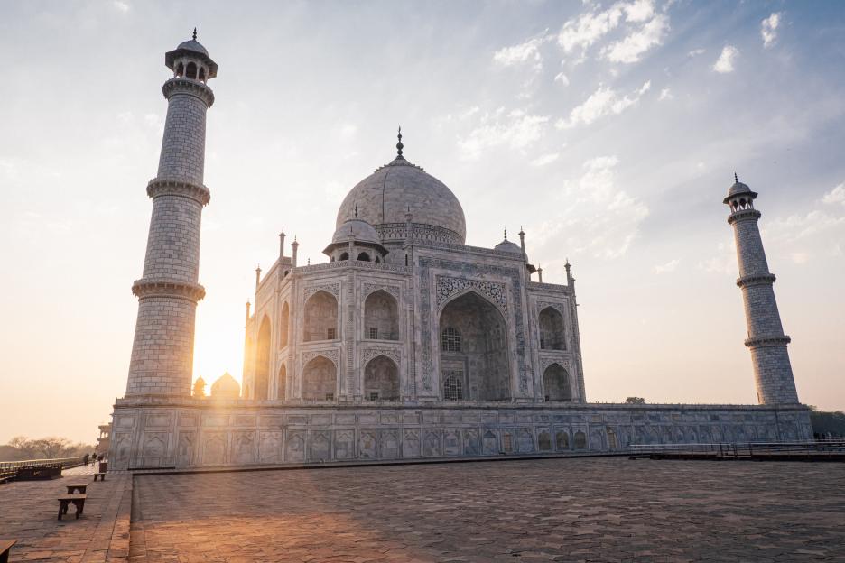 The Taj Mahal at sunrise, with a large white marble mausoleum and two minarets under a clear sky.