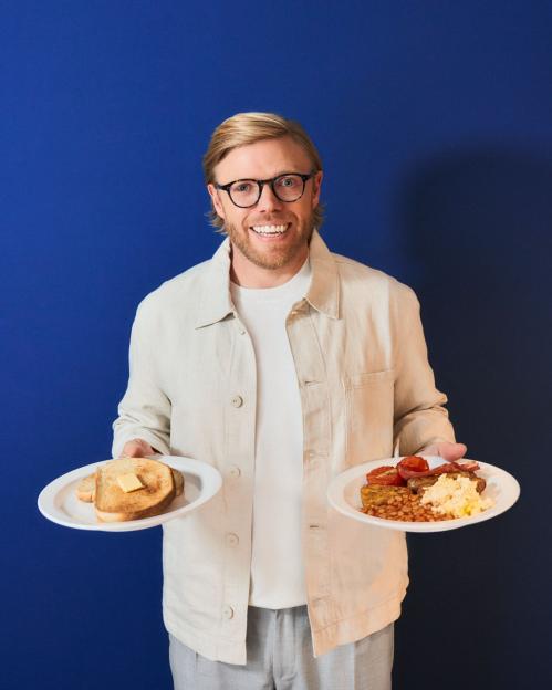 Man holding a plate of toast and a plate of full English breakfast.