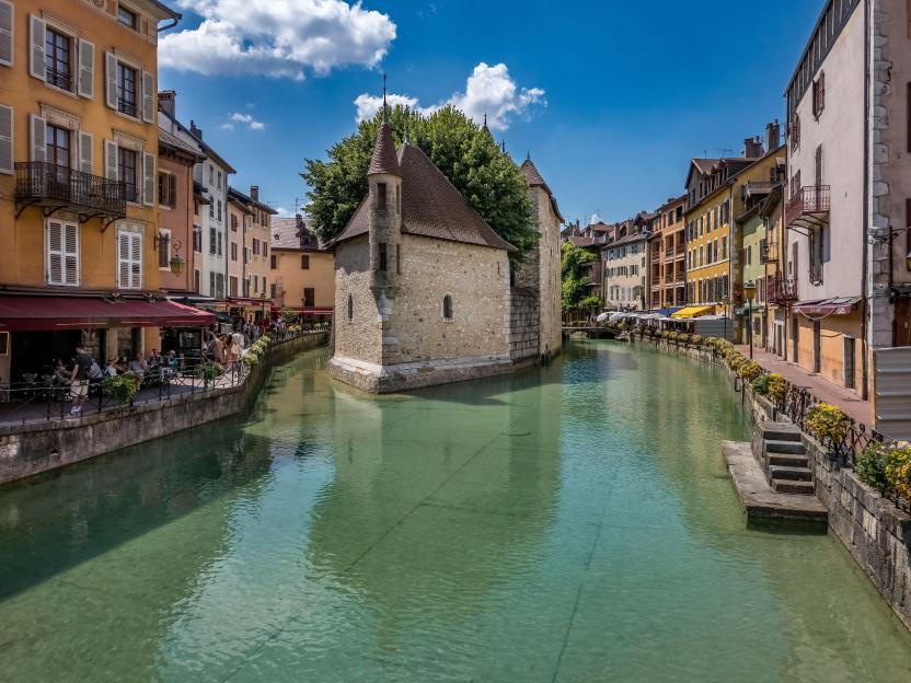 The Palais de l'Isle, a former prison and castle, situated in the medieval downtown of Annecy, France, with a blue cloudy sky.
