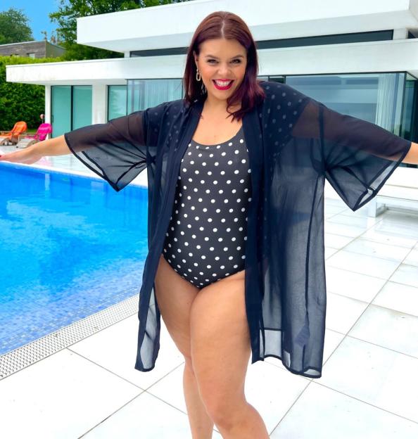 Woman in a black polka dot swimsuit and sheer black kimono by a pool.