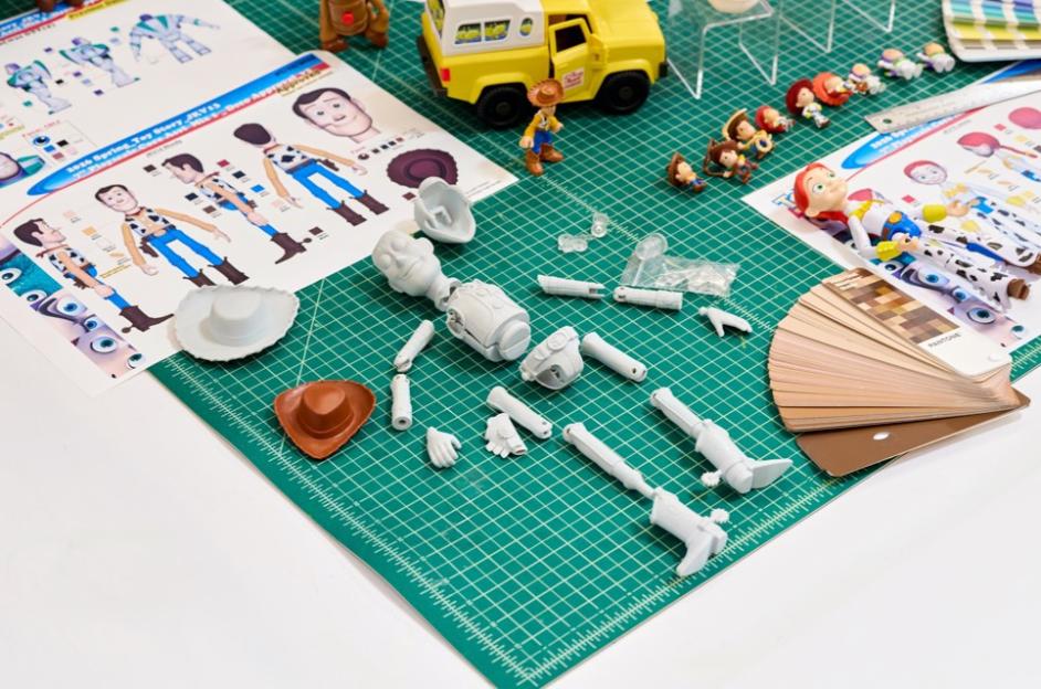 Toy Story character models, design sheets, and miniature figurines on a green mat.