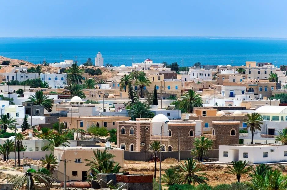 Elevated view of Guellala town in Djerba, Tunisia, featuring low-rise buildings and palm trees against the backdrop of the blue sea.