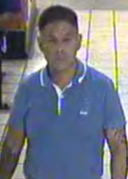 Image of a man with short dark hair, wearing a blue polo shirt with a white collar and white trim on the sleeves, and tattoos on his arms.