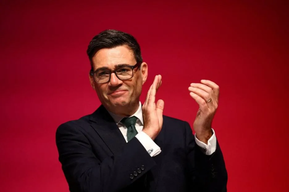 Andy Burnham clapping in front of a red backdrop.