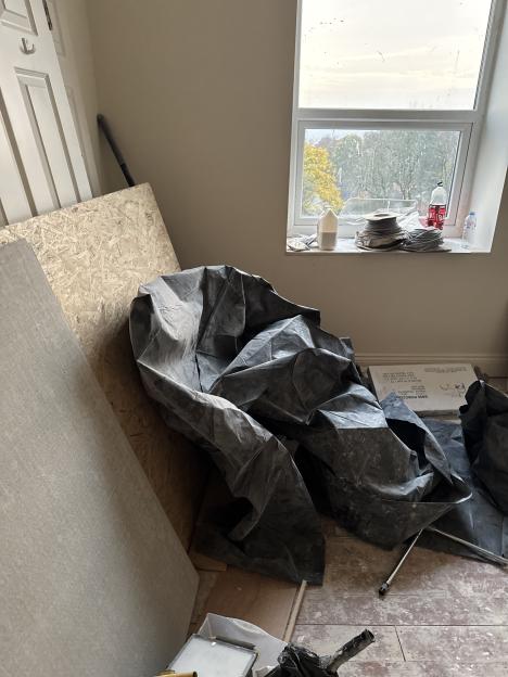A room under construction with building materials, a window, and plastic sheeting on the floor.